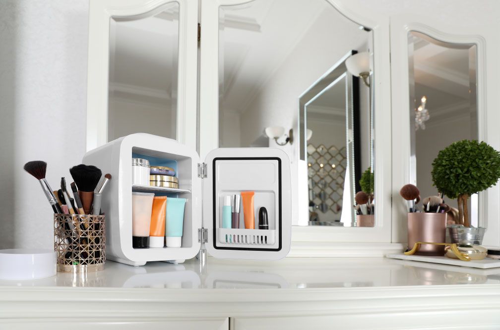 Mini fridge with cosmetic products on white vanity table